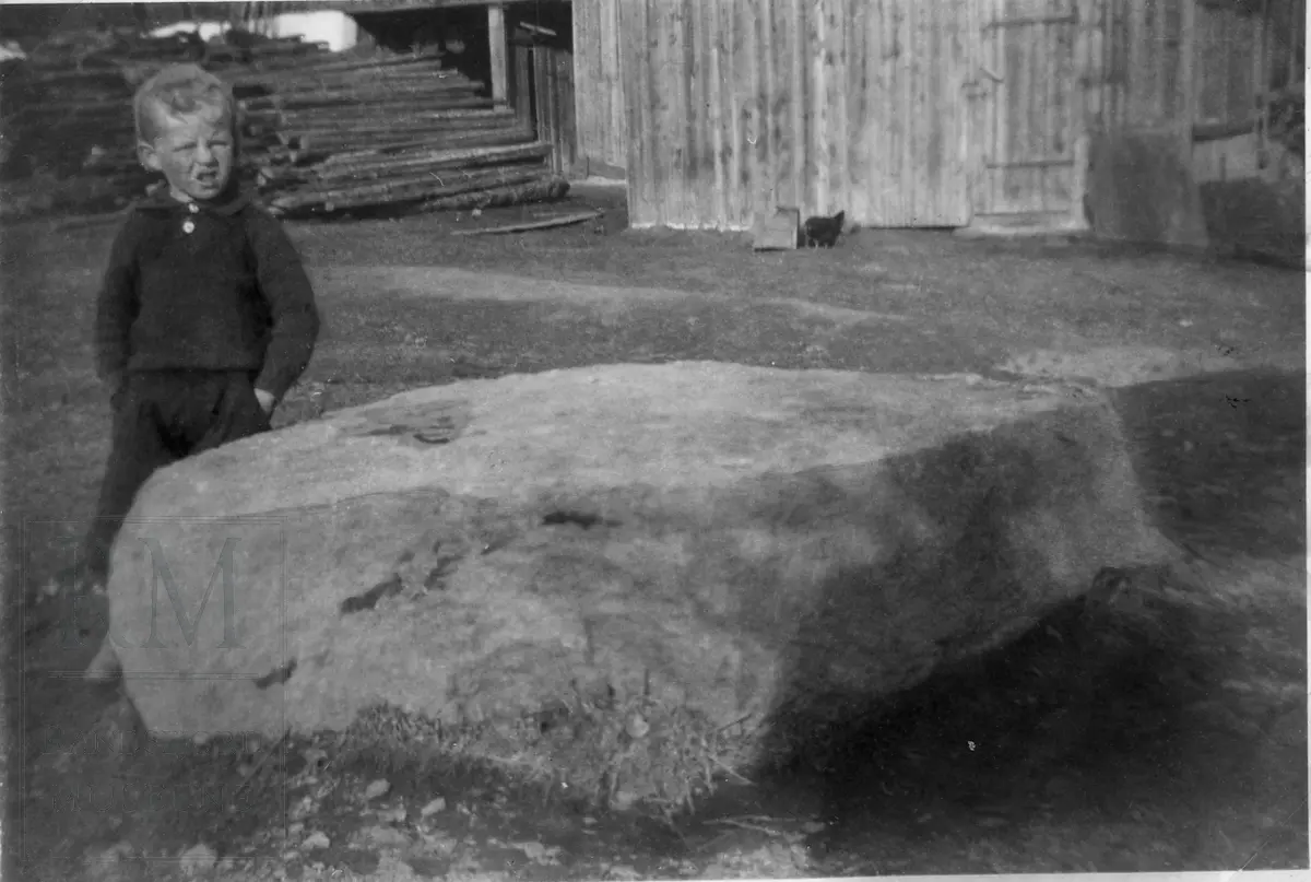 En liten gutt stående ved en stor stein.