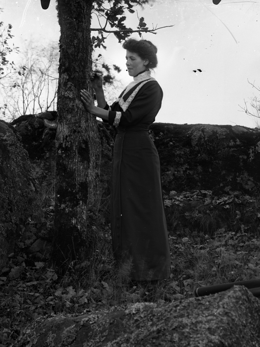 Kvinnoporträtt. En kvinna fotograferad utomhus stående vid ett träd.
