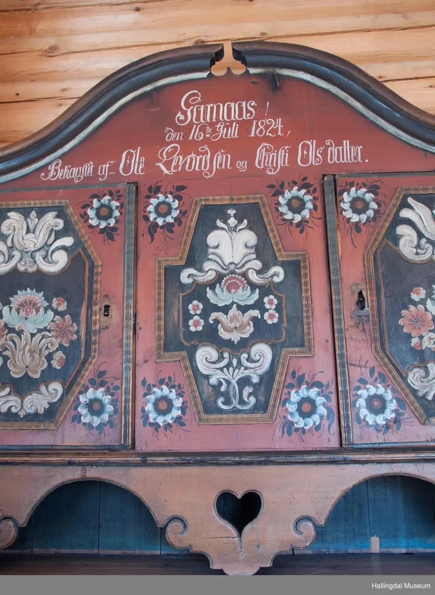 Delene festet med trenagler.  Høy, buet gavl med fremspringende kronlist som øverst har gjennomskåret omvendt hjerte.  Kronlist har hulkil og vulst, og fortsetter på sidene av overskap.  Overskapets front delt i tre felt, med en dør i hvert sidefelt.  Dørene er hengslet til skapets sider.  Hengslene av jern og festet på overkant og underkant av skap og på overkant og underkant av ramme.  Dørene har to profilerte labanker i spor på innsiden.  Låskasetter innfelt i dørblad.  Låsskiltene mangler.  Nøkkel med kløverformede hoder, profilert. En skillevegg midt i overskapet.  To hyller i hvert skap.  Dørene og midtfelt har speil med fyllinger og utskjæringer, akantus i relieff på speilflatene.  Dørspeilene er ovale, åttekantede.  Speil i midtfelt har tilnærmet korsform.  Skjenken har utskåret forplate, i tunger.  Under midfelt får forplaten helt ned til skjenkeplate med gjennombrutt hjerte.  Halvrunde åpninger i hver side. ..........