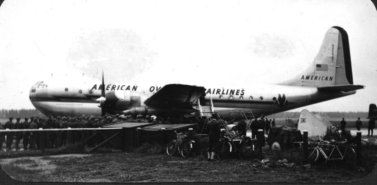 En, Boeing "Stratocruiser" fra American Overseas Airlines parkert med flere Trandum-soldater som står i kø for å slippe ombord.