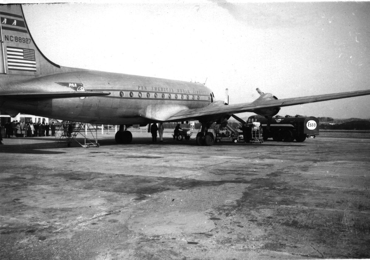 Lufthavn/Flyplass. Et fly, Douglas DC6 fra Pan American World Airways, parkert. En tankbil fyller drivstoff og passasjerene må vente på ombordstigning.