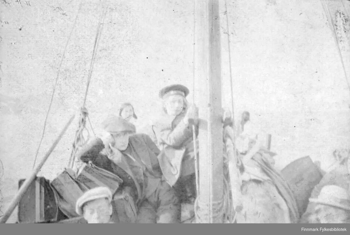 "Paa Tanafjorden 1917". Vi kan skimte 3 personer ombordi en seilskute. I front av bildet ser vi hodet på en mann med skyggelue/sixpence. Bak sitter det en gutt og lener hodet på ene hånden, han har sixpence og frakk, med dressjakke, genser og bukse under frakken. Ved masten står en gutt og holder seg fast, han har matroslue og en tykk frakkeliknende jakke. Helt bakerst skimter vi omrisset av et hode, muligens en kvinne. Til venstre i bildet ser vi også bagasje, mulighens kofferter. Nede i høyre hjørne kan man ane et hode med lys hatt og hattebånd.