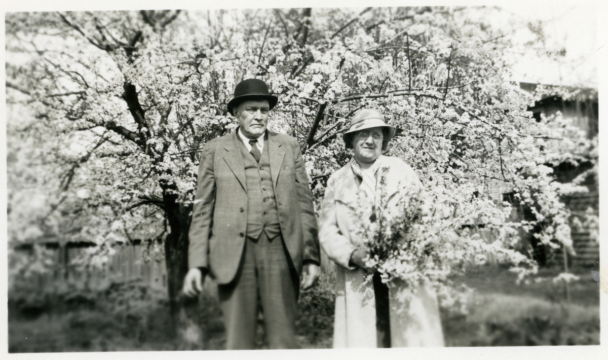En mann og en kvinne foran et stort blomstrende tre. Kvinnen holder en bikett blomster i hendene.