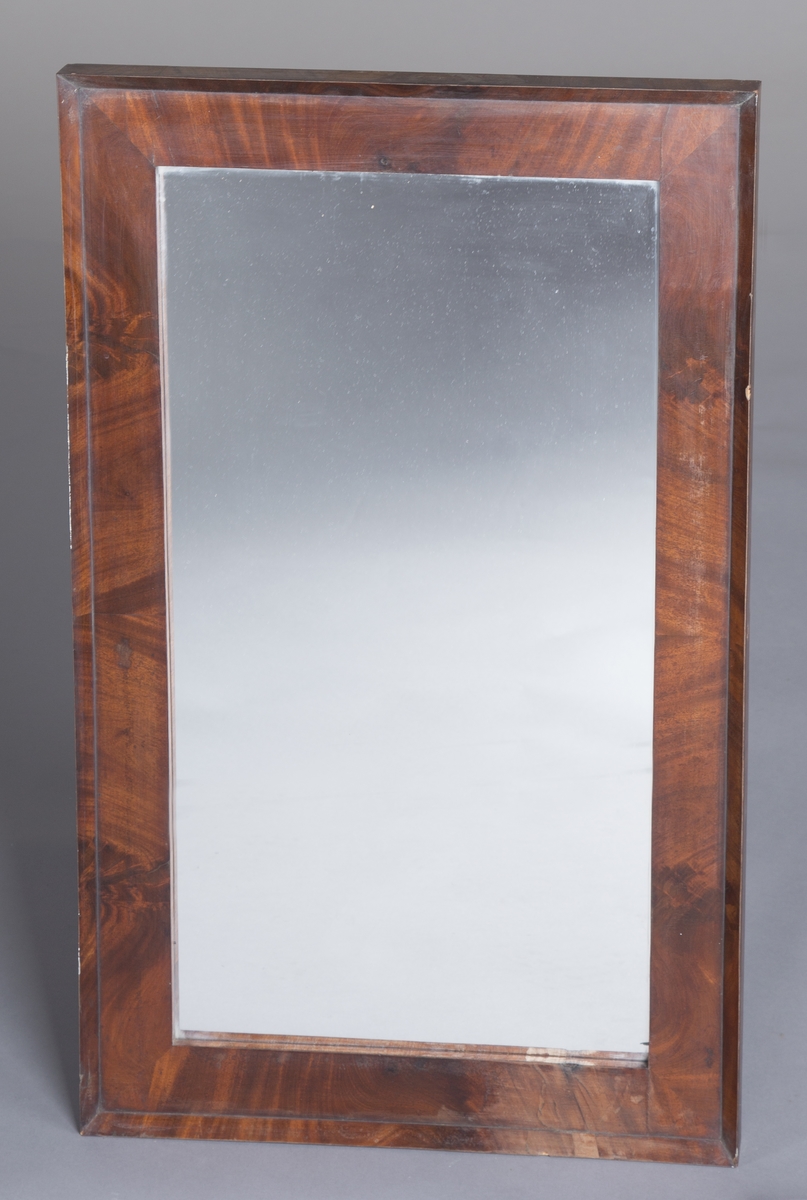 Rektangulært speil med treramme. Rammen har trolig mahogny-finér og er lakkert. Stram, enkel utforming.