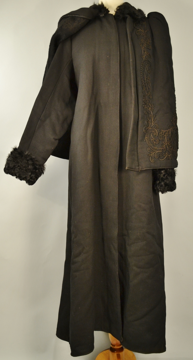 Kåpen er helforet med silkefor. Den består av kåpe med en fastmontert cape. Den er dekorert med lissebroderier i silke på krage og cape.