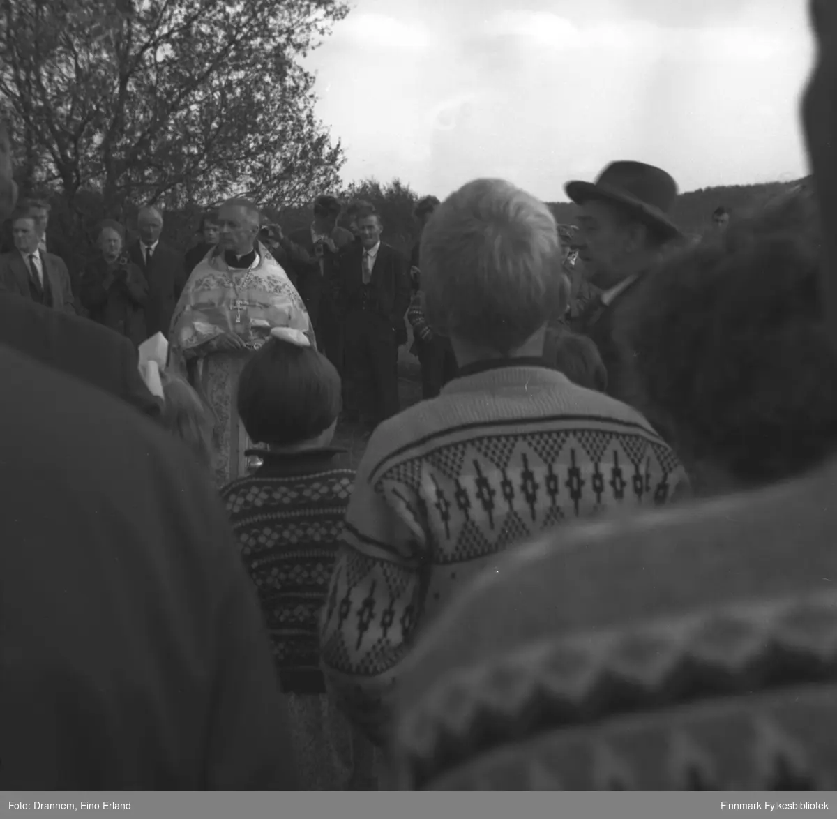 En kirkelig mann står på en lysning med mange personer rundt seg.