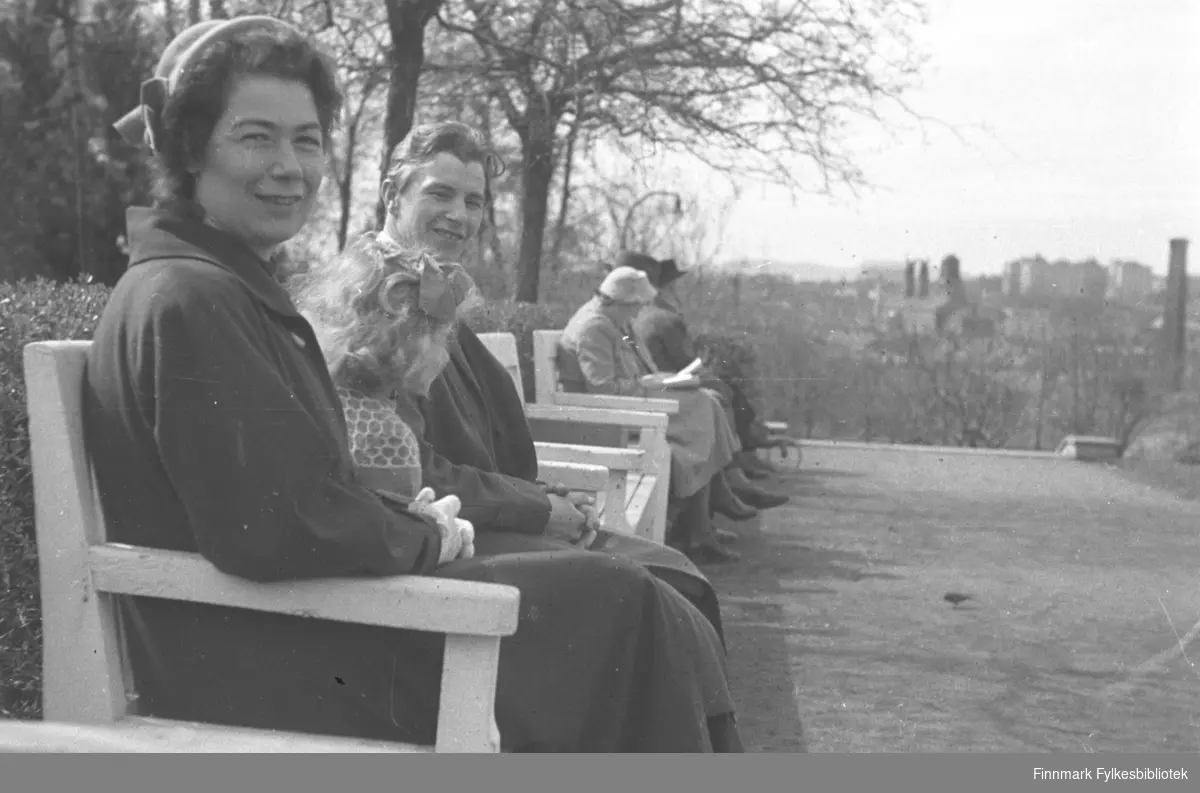 Familien Drannem sitter på en benk i en Park, Jenny nærmest kamera, Eino bakerst og Turid i midten. Bidet er tatt i Oslo.