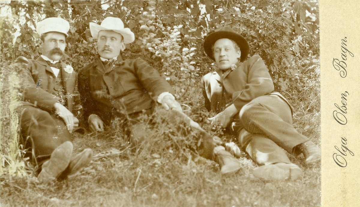 Portrett av Hans, Olaus og Ola Islandsmoen liggende i gresset, alle med hatt på hodet.
