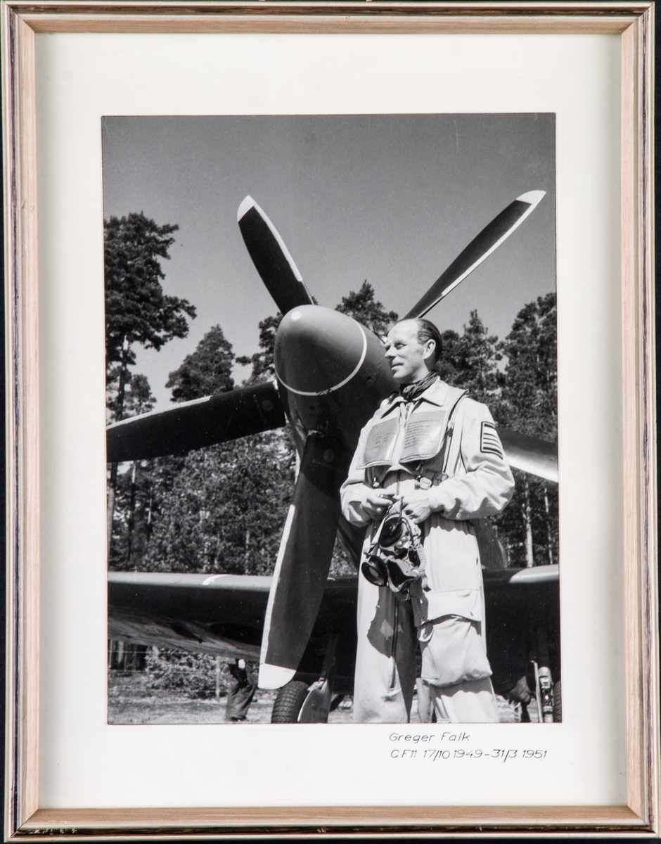Porträttfotografi av Greger Falk, chef för Södermanlands flygflottilj i flygardräkt vid flygplan S 31. Inramat foto.