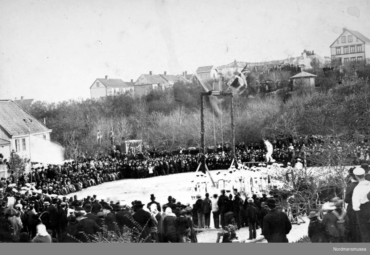 Det første Romsdalske turnstevne på Latinskoleplanen på Barmanhaugen, Kirkelandet i Kristiansund trolig året 1892. Her ser vi publikum i ring rundt turnerne (i de hvite draktene) og turnstativet. I bakgrunnen ser vi Barmanhaugen. Fra Nordmøre Museums fotosamlinger.