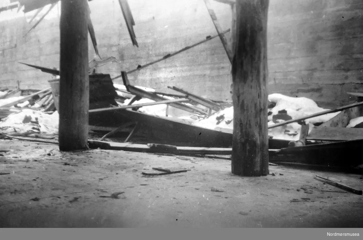 Museets gamle torskegarnbåt (katalog nr. 9/1935) og katalog nr. 646) - geitbåt fra Williamsen på Indre Flatset, Frei - opprinnelig kirkebåt - knust under snømassene da taket gav etter i Johnsenbrygga på Skjerva. Bildet viser snøhaugen med restene fra taket og båten stikkende opp fra snøen. Alle bildene i denne serien strekker seg fra 1947/882 til 1947/885.(KMb-1947-000.0882.jpg osv.). Bildet er datert Mars 1947. Serie. Fra Nordmøre Museums fotosamlinger