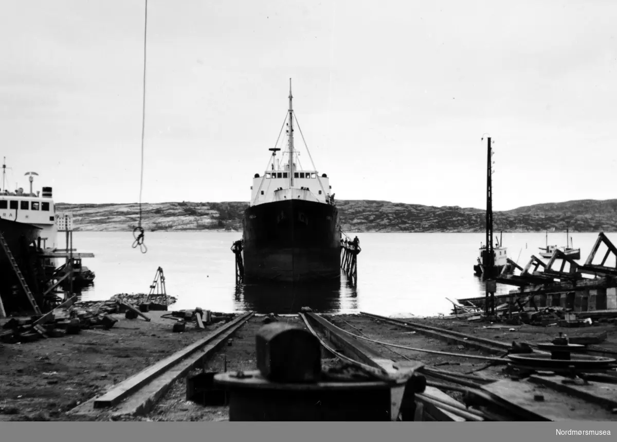 Bildet er fra Storviks Mek. Verksted og slippsetting av Ole T. Flakkes lastebåt M/S";Knoll"; på den nye patentslippvogna klinkbygget i stål 1918, den største slippen mellom Bergen og Trondheim, og erstattet med nytt slippanlegg ca. 1979. Til venstre på beddingen ses B/F";Norddalsfjord" verkstedets bnr.14.



"Norddalsfjord" ble levert til Møre og Romsdal Fylkesbåtar 15. mars 1961 og hadde følgende hoveddimensjoner: L 31,20 m x B 8,55 m x D 3,35 m og hadde en tonnasje på 159 bruttoregistertonn. Fremdriftsmaskineriet består av 3 Volvo Penta turboladede dieselmotorer type TMD96 på til sammen 420 hk som via kilremdrift var koblet til et felles gir og propellaksel med vribar propell, slik at hver enkelt av motorene kunne kjøres separat. Fergen hadde 2 Bolinders vekselstrømsaggregater type 1052MG på 23 hk hver tilkoblet en generator på 17 kW. Fergen var utstyrt med elektrohydraulisk styremaskin. Fergen har plass til 18 personbiler og har sertifikat for 160 passasjerer. Forut er det innredet 6 lugarer for offiserer og restaurantpersonale og akterut en mannskapslugar for 4 personer og toppfarten er 11,4 knop og marsjfarten 10,5 knop. Ferga er verkstedets første nybygg etter B/F"Trygge" som ble levert i 1938.

Bak nybygget ved piren ligger B/F";Eira"; fra MRF for puss og vedlikehold.Utenpå B/F";Eira"; ligger verkstedets slepebåt M/B";Havna"; som regel ført av Kåre Frisvold. M/B"Havna" ble kjøpt fra Backer på slutten av 1940-tallet og Backer hadde i 1946 fått installert den siste Sterkodermotoren (oppfyringmotoren) og båten ble populært kalt "Molloksen" og den ble kondemnert i 1959. Til høyre, over såpehellingen bak stålmasta, ses dykkerbåten til A/S Anlegg i Trondheim i ferd med å reparere slippbanen ute i sjøen. Litt til høyre for dykkerbåten ses fiskeskøyten til fisker Olaf Olsen på Dale, som ligger i utlegget sitt og foran dykkerbåten ses såpehellingen fra 1901. I forgrunnen, til høyre, ses kasteblokka til den nye patentslippens opphalingsspill. I bakgrunnen ses Skorpa og helt i høyre kant, over såpehellingen, ses en bit av "Høttnesbrygga". Bildet er fra 1960. Kilde:
Peter Storvik. Fra Nordmøre museums fotosamlinger.
