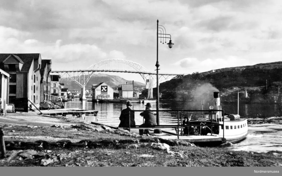 Sundbåten legger til på Gomalandet. I bakgrunnen ses Nordholmen under broa og til venstre brygger på Gomalandet. Til høyre ses Nordlandet i Kristiansund.
Bildet viser sundbåten ”Fram”som  ble bygget i 1878 ved Trondheims Mekaniske Verksted og var 11,7 meter lang, 2,5 meter bred og hadde en tonnasje på 15,38 bruttotonn. Båten ble senere sertifisert for 45 passasjerer og ble satt i drift 17. juni 1878. Ved utbruddet av andre verdenskrig ble ”Fram” senket under bombingen 28. april til 1. mai 1940. Båten ble hevet 8. mai og satt på slipp ved Sterkoder Mek. Verksted, for så å bli reparert der i 1941. Båten opphørte i drift da formannskapet den 21. august 1958 vedtok å overdra ”Fram” vederlagsfritt til Havnevesenet som arbeidsbåt. 
Kilde for båtene: Sven Erik Olsen og Tor Olsen. Sundbåten. Folk over havna - fra fergemenn til Angvik. Utgitt 2005. (Info Peter Storvik). --
Et bilde av en sundbåt som nettopp har lagt til kai på Gomalandet i Kristiansund. På brygga ser vi to menn sitte på en benk og se i retning mot Nordsund bru, som knytter Gomalandet sammen med Nordlandet. Nordsundbroa stod ferdig i desember 1936. Fra Nordmøre Museums fotosamlinger.