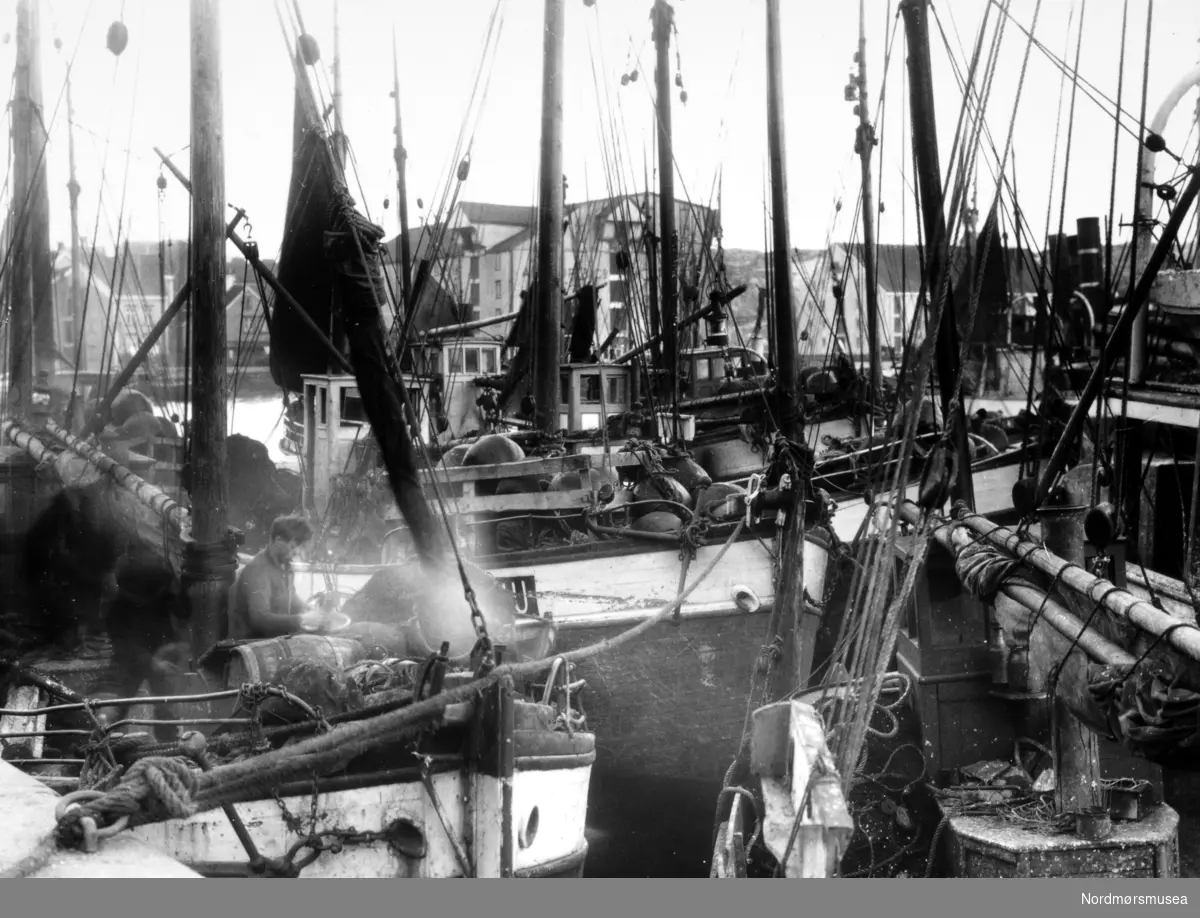 Foto nr. 25728 fra Anders Beer Wilses fotoarkiv, hvor vi ser deler av fiskeflåten liggende ved Johnsenhuken i Kristiansund. Fotoet er fra perioden rundt 1910-1930. Fra Nordmøre Museums fotosamlinger.

