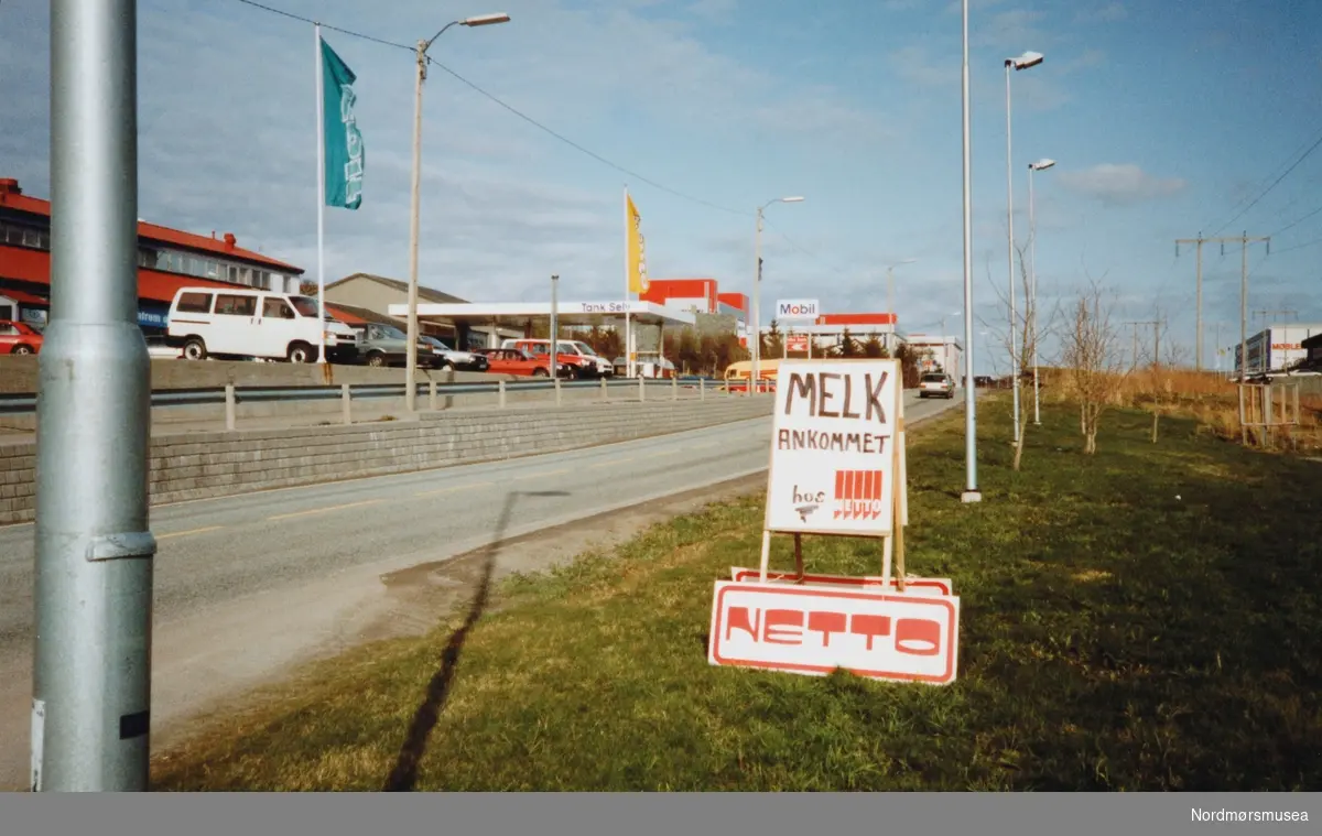 Foto fra Løkkemyra, hvor vi ser at butikken Netto minipris reklamerer med at melk er ankommet butikken. I bakgrunnen ser vi ellers blant annet bensinstasjonen Mobil. Bildet er tatt i forbindelse med nyttårs-orkanen i 1992. Fra Nordmøre Museums fotosamlinger.
