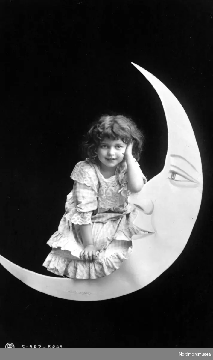 ";S-582-5845"; Arrangert studiobilde med en ukjent ung pike, her sittende på en smilende ";halvmåne"; oppe på himmelen, med natten i bakgrunnen, muligens iført en nattkjole? Piken kan være fra Kristiansund, eller med tilknytning til Nordmøre. Fotograf er ser ut å være R. P. H. ? Datering er mer usikker, men er trolig fra perioden 1900 til 1910.studiobilde, halvmåne, scenedekor, pike, jente, klær, mote, nattkjole
 
Fra Nordmøre Museums fotosamlinger.
