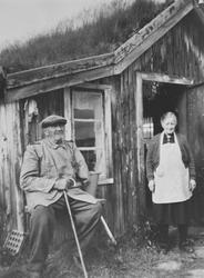 Portrett av eldre ektepar foran eldhuset på setra Pustbakken