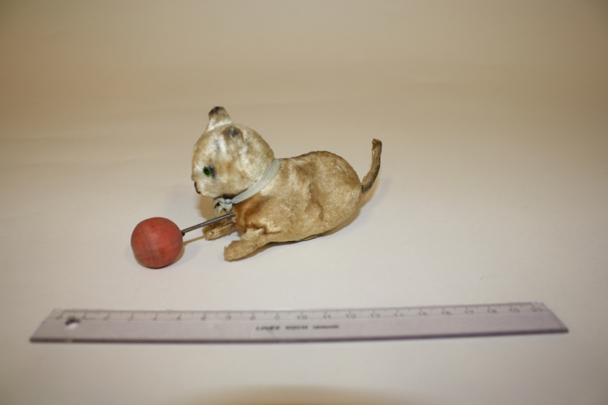 Gitt av Lisbeth Andreassen Chumak. Liten katt med ball og sløyfebånd. Ballen er festet til katten med stålstreng. Fra 1950 tallet.