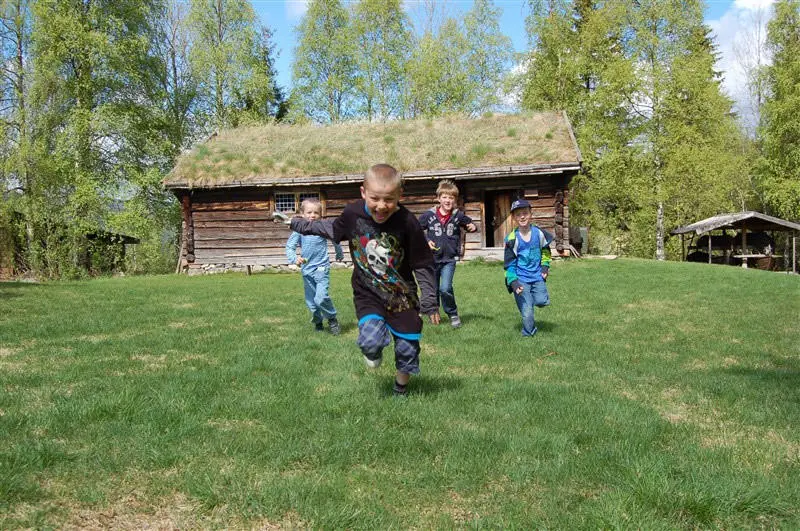 Barn løper mot kamera. De løper foran Eriksstugua  mot kamera på Trysil Bygdetun.