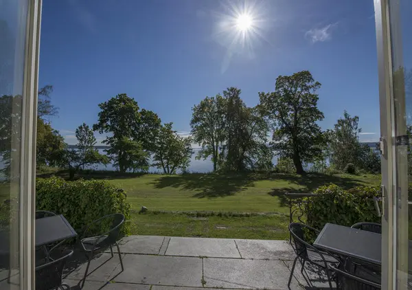 Utsikt over stor gressplen og Mjøsa fra verandaen på Storhamarstuene.