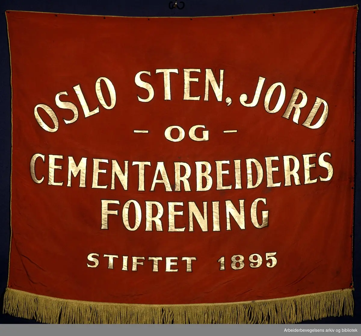 Oslo sten- jord- og cementarbeideres forening.Stiftet 15. februar 1895..Forside..Fanetekst: Oslo Sten, Jord og cementarbeideres forening..Stiftet 1895..Baksiden er lik