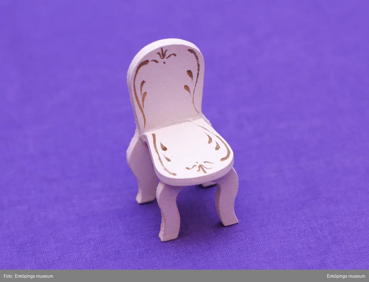 Vitmålad stol med gulddekor på säte och rygg.