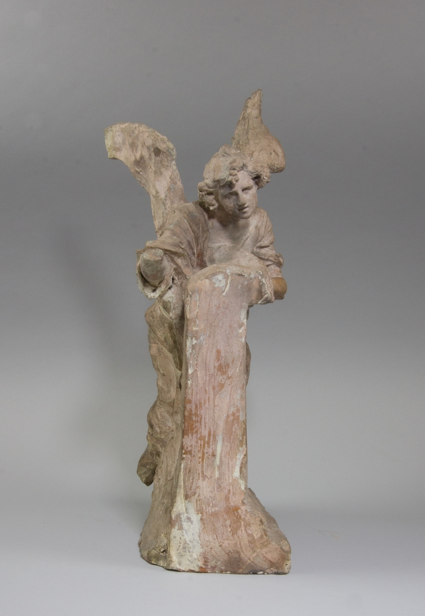 Knäböjande ängel i helfigur som lutar sig emot en arkitekturdetalj delvis täckt av en textil.