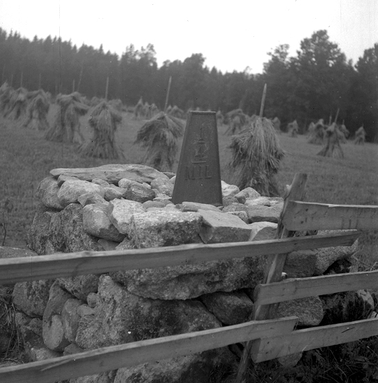 Foto av en milsten av järn, med röse. 
Text: "1/4 MIL."
I bakgrunden syns det en åker med kärvar.
7000 m SSÖ om Älmeboda kyrka. 0,5 m V om vägen.
Vägen Rävemåla-Yxnanäs-Gränsen.
Källa: Kronobergs läns väginventering 1943.