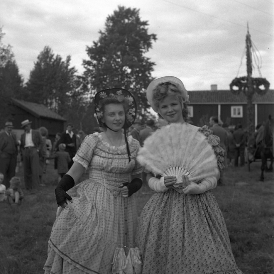 En midsommarstång med två utklädda unga kvinnor i förgrunden.