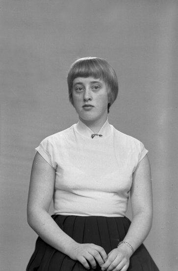 Foto av en ung kvinna i blus och kjol.
Midjebild. Ateljéfoto.
Britta Petersson, Mo Gård, Östregård, Hjortsberga, (1941-  ). Bosatt senare i Lekaryd.