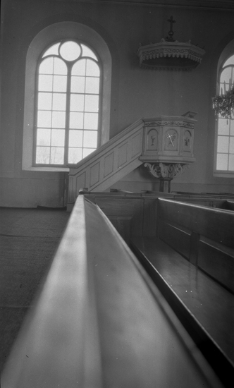 Foto på en predikstol med kyrkbänkar längst fram i bild.