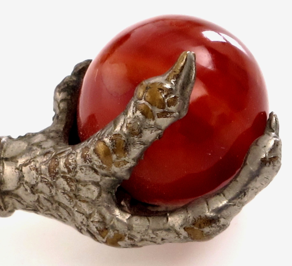 En ørneklo, denne griper/ om en kuleformet rødbrun polert sten.
