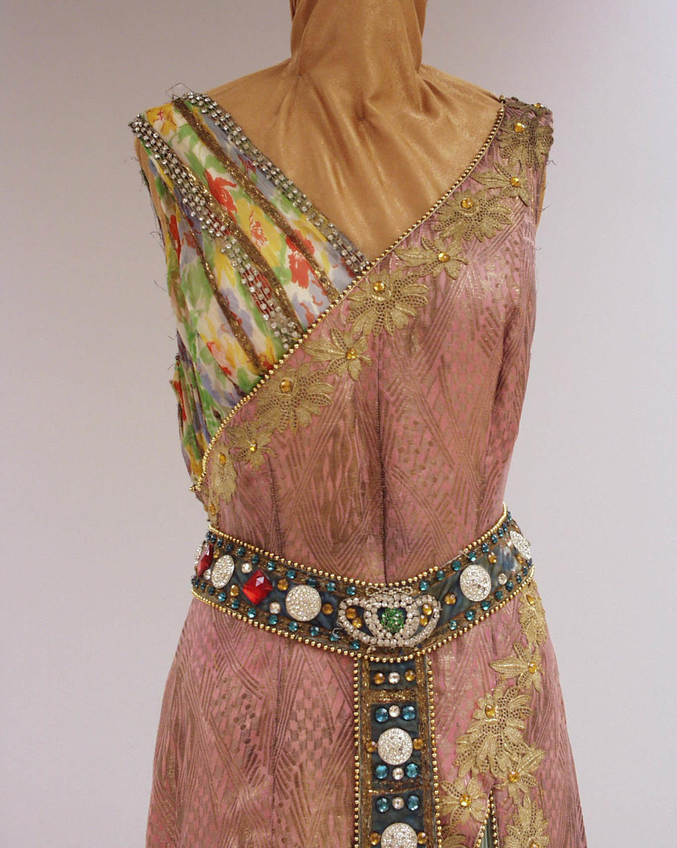 Rosa kjole med flere detaljer og farger. Stort belte rundt livet med detaljer nedover front på kjolen.