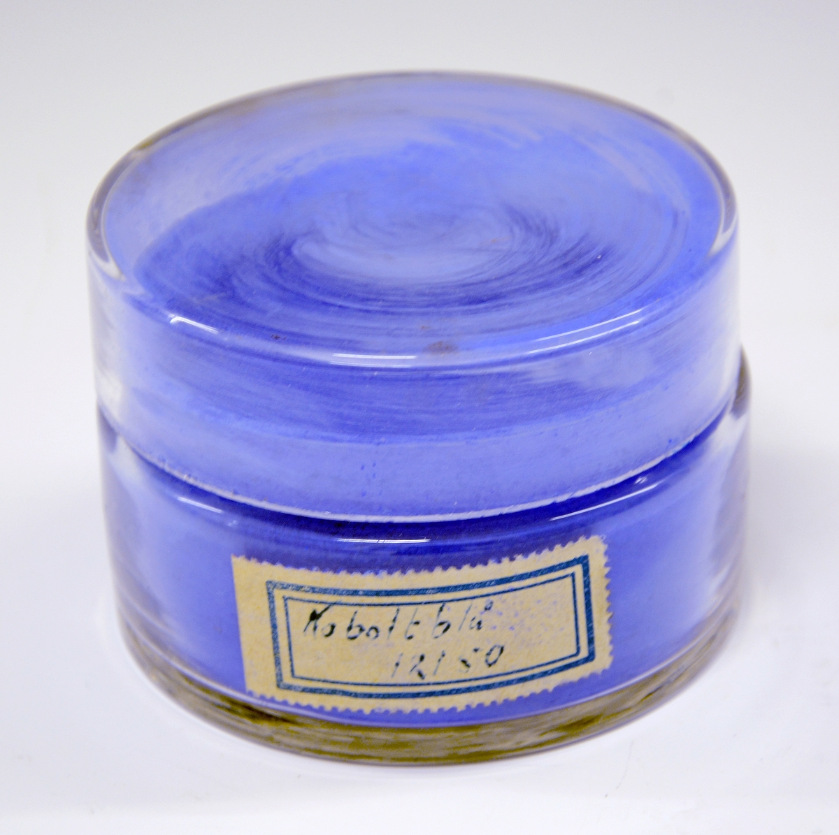 Krukke med lokk i glass. Beholder til fargepulver  brukt i dekoravdelingen ved PP. Fylt med koboltblått fargepulver.