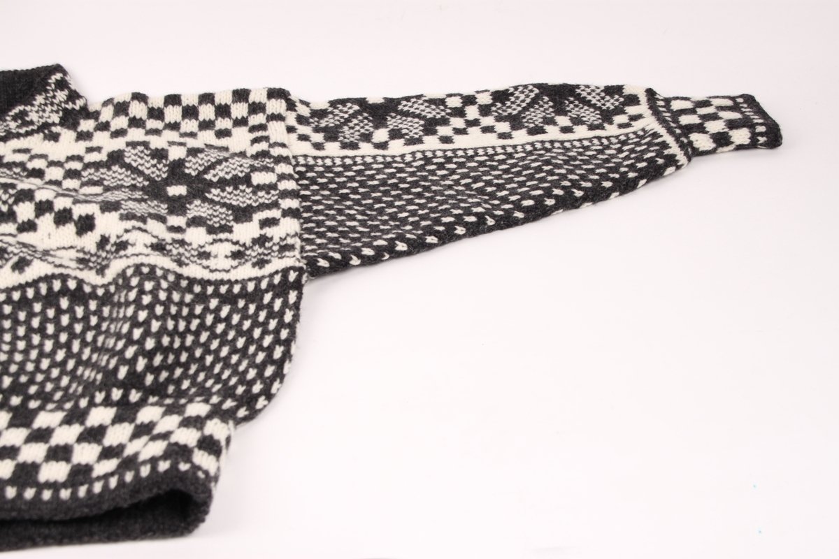 Håndstrikket ullgenser i svart og hvitt garn. Hele genseren er mønstret med åttebladsroser, blomster, ruter og doble lus.