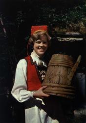 Postkort. Ung pike i Hardangerbunad. Bærer på en ølkanne fra