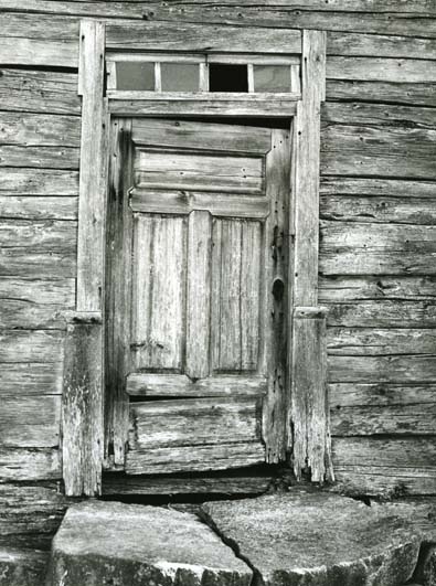 Dörren till bagarstugan vid gården Ersk-Mats i Hassela. Dörren är sliten och i överljusfönstret ovanför dörren saknas en ruta.