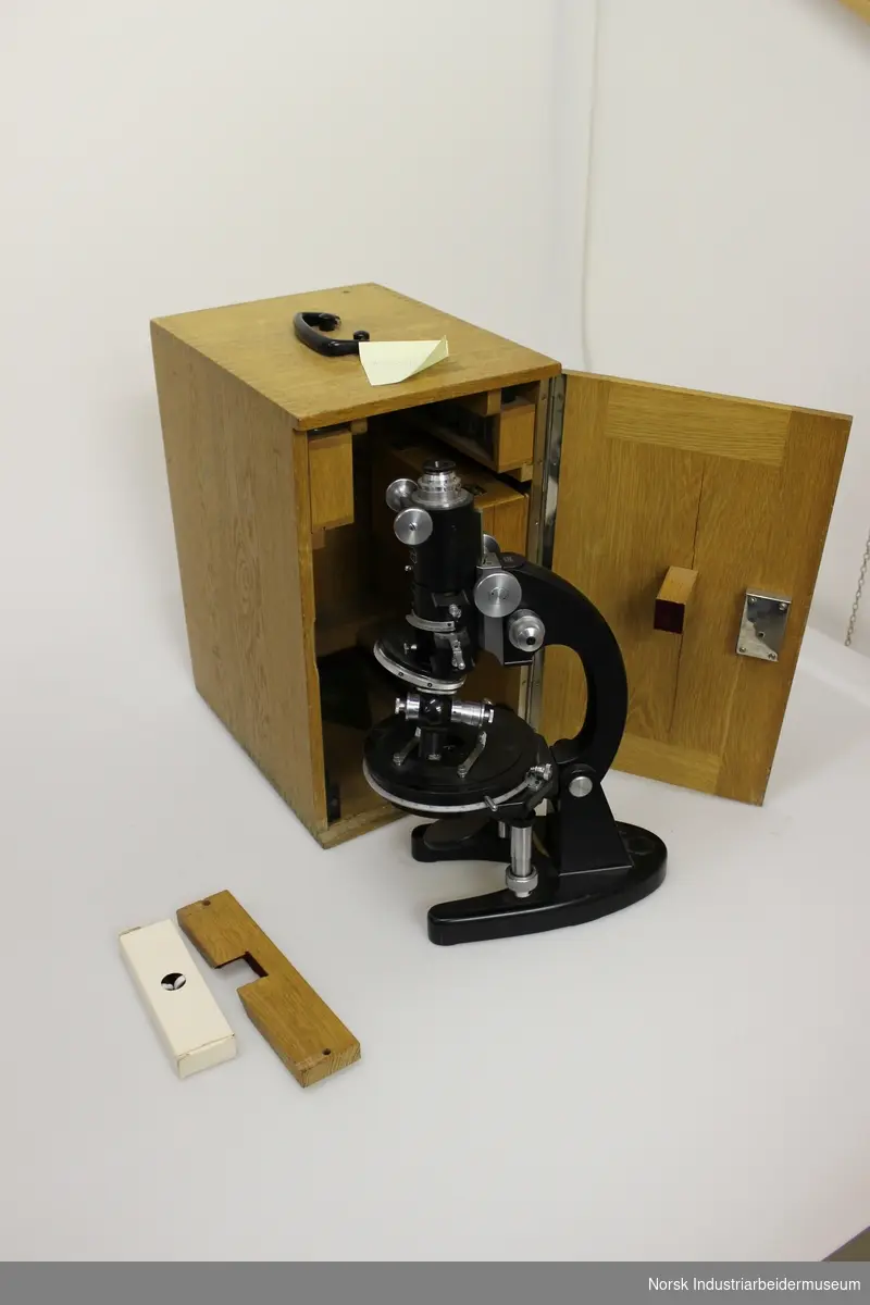 Mikroskop med trekasse.
Mikroskopet har to linser merket med h.h.v. 3 og 6
Oppbevares i en nøttetrekasse som inneholder en del  tilleggsutstyr, s.s. glassplater, etc. 
Dimensjon: 31x13,5x14 cm