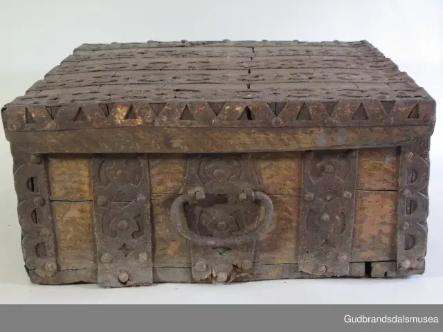 "Rik gjenombroten jarning over heile skrinet. Gamal type, alder uviss. Fra Vestre Gausdal". (Jf. "Katalog for Lom Bygdesamling,1925"). 
Skrinet har 3 rom, nøkkelhullslås og jernhandtak på sidene. Lokket er satt sammen av 2 bord, er festet til utsiden på bakstykket med to hengselbeslag og har 2 sidelister festet med trenagler. Bunnen er satt sammen av 2 bord, festet til hverandre med 2 forsenka trenagler; bunnen er festet til skrinrammen med trenagler.  Skrinrammen er tappet og forsterket med hjørnekantbeslag utvendig. 
Skrinet har jernbeslag med gjennombrutt mønster, 5 stk. B: 6,5 x L: 45 cm på lokk, 3 på hhv. bakstykke, front og sidestykker B: 6,5 x 20 cm. Lokket har ett låsbeslag og de to øvre hengselbeslag festet på innsiden, de to nedre hengselbeslag er festet på utsiden av bakstykket. Alle beslag er festet med store jernnagler samt festet under bunn på skrinet. De to hengselbeslag har også gjennombrutt mønster.  Nøkkelhullslåsen mangler låsanordning på innsiden.
DEKOR. Malingen har blitt beskyttet med et lag ferniss el.l., noe som ble vanlig fra begynnelsen av 1700-tallet. Ingen skurddekor. I stedet er beslag av jern brukt som dekorelement, noe som periodemessig kan peke på 1600-tallet, tidlig 1700-tallet, der treskurden ikke var fremherskende. Liknende dekorbruk finner du på LBY0328. Skrinet har gjennombrutt mønster på beslag og store jernnagler som beslagfeste. Treverket som synes mellom beslagene er malt med horisontale bølgestrukturer i gul og brun. Den dominerende dekorfargen er brun og gul, men det finnes små rester av blå eller blågrønn på lokk, sidelister på lokk, front og bunnkant på bakstykket samt av gul på frontbeslag. Innsiden av lokket er malt i terracottarød nyanse. Tradisjonelt fremkom denne fargen ved bruk av saft fra orr blandet med spytt, som ble smurt ut over treet. 
BRUK. Før kofferten kom i bruk hadde man reiseskrinet, som ble brukt til oppbevaring av bl.a. klær, verdisaker og mat på reiser. Skrinet hadde ofte et eller to mindre, smale rom langs den ene skrinsiden og ett større rom. De fleste reiseskrin var i tillegg forsterket med jernbeslag langs alle kanter og med en solid nøkkelhullås til sikring mot støt, slag og tyveri.
