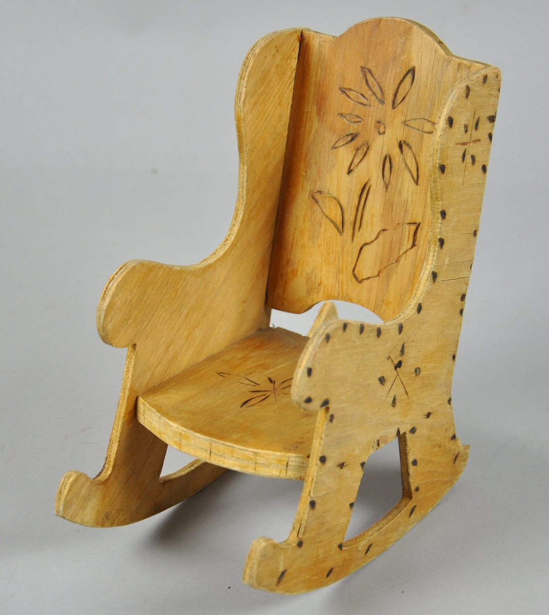 Dukkestol laget av finér. Stolen har svidekor i rygg, sete og sidestykkene.