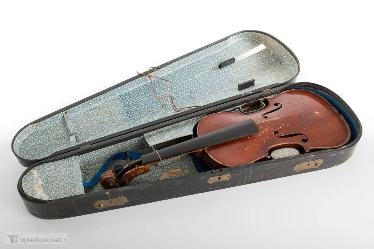 Brunlakkert fiolin. Mangler bue og strenger og fingerbrettet er løst.
Mest sannsynlig en kopi av en Stradivarius fiolin fra 1800- tallet, en såkalt "tyskerfele" eller "dusinfele".
(Se opplysninger for mer informasjon)

Svart fiolinkasse kledd med dekorert papir og kledd med blå filt i bunnen. Et lite rom i forkant for div. ekstrautstyr. Utstyr med lukkemekanisme foran og bak, og lås i messing. Håndtak av messing på toppen av kassen.
