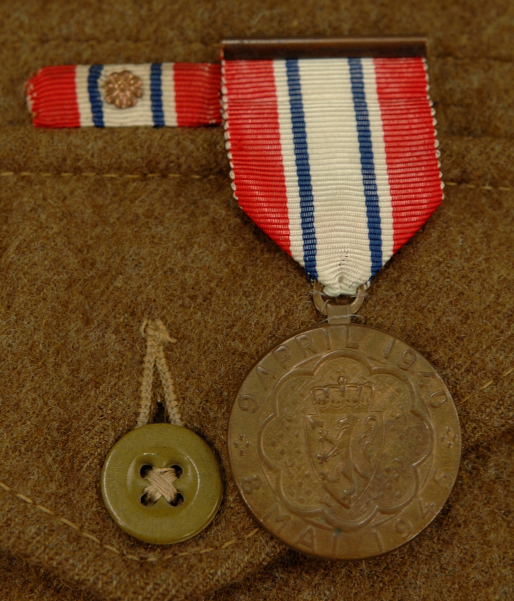 Uniform som består av: Jakke med armbind, bukse, lue/barett, belte og gamasjer/anklets.

Uniformen er i vadmel og militærgrønnfarge. Armbindet er i strie med det norske flagget påsydd. Armbindet er påsydd venstre arm.

Jakka er kort, str. 9. På innsiden er det trykket stoffmerke. Over ytterlommen sitter det ei medalje og eit rektangulært flagg med ein metallrose på midten.

Buksa har 2 lommer foran og 1 bak.

Lua/baretten har bomullsfôr inni. I front på lua sitter Haakon 7'merke med lauvbærkrans rundt.