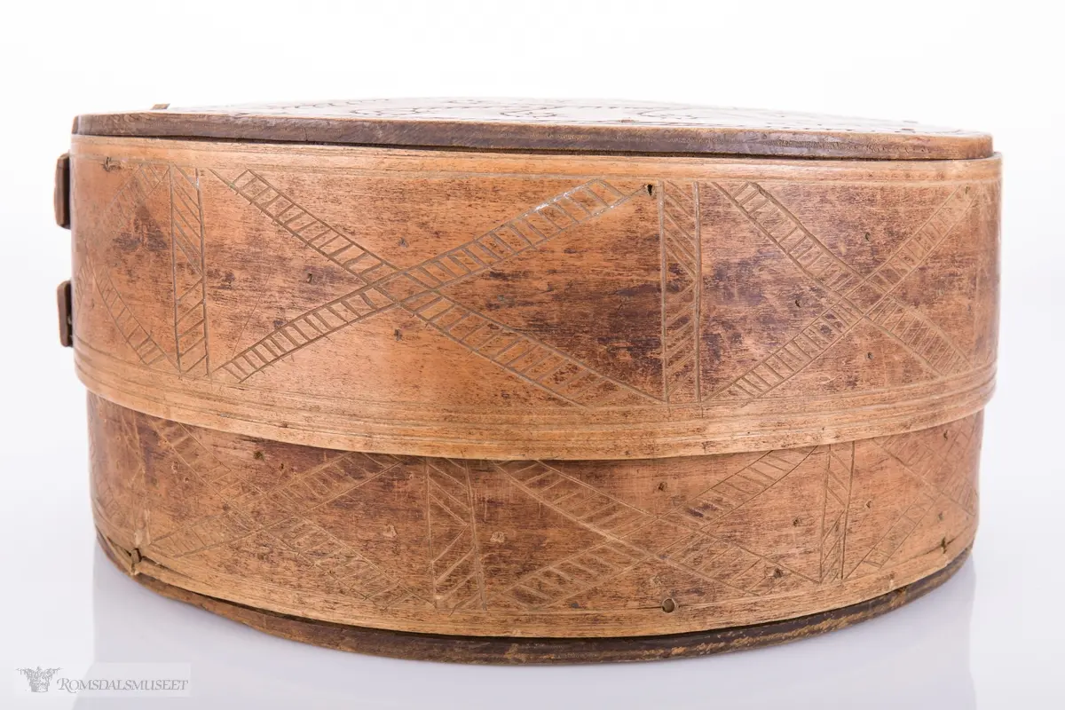 Eit kvistmønster/bregner på lokk. Skravert kryss- mønster langs trosken. Rosett av spetter i bunnen.