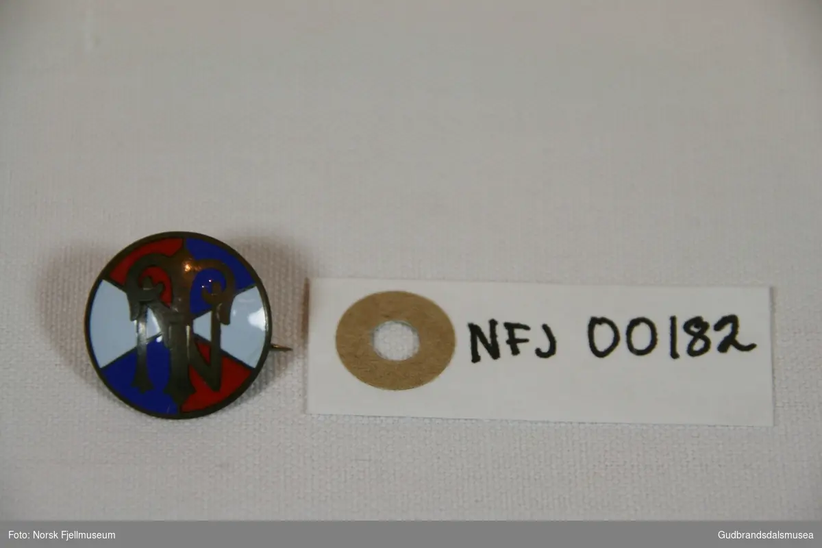 Medlemmsmerke fra DNT. Sirkelformet med logo på framsiden og nålfeste på baksiden.