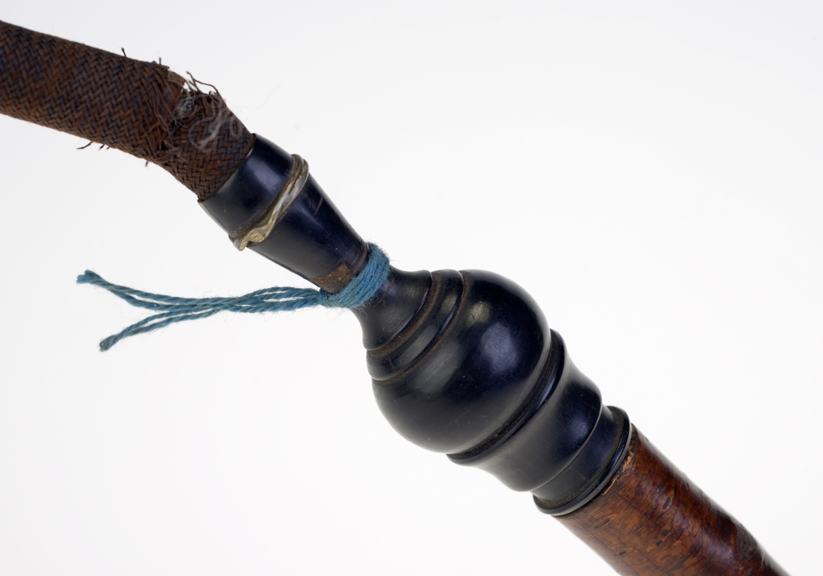 Et piperør med munnstykkke som har tilhørt en langpipe. Piperøret er laget av løvtre som har barken på og er mørk brun på farge. Nederst er røret spisst/tilspisset. Øverst er festet til munnstykket. Det er laget av ibenholt og er kuleformet. Øverst på denne er det lagt inn en stripe med sølv. På denne delen er det også surret en blå tråd. Deretter er det en metallspiral kledd med tekstil som er bøyelig. Til sist er munnstykket som er laget av bein og brungrå på farge. Det har enkel dekor i form av en ring som er skåret ut.