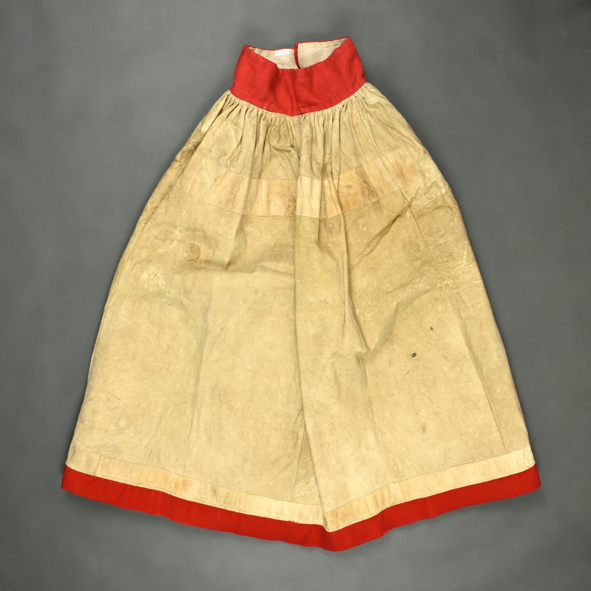 Kjol i skinn med pälssidan inåt som är sydd i fyra våder med rött kläde i linning och nertill.