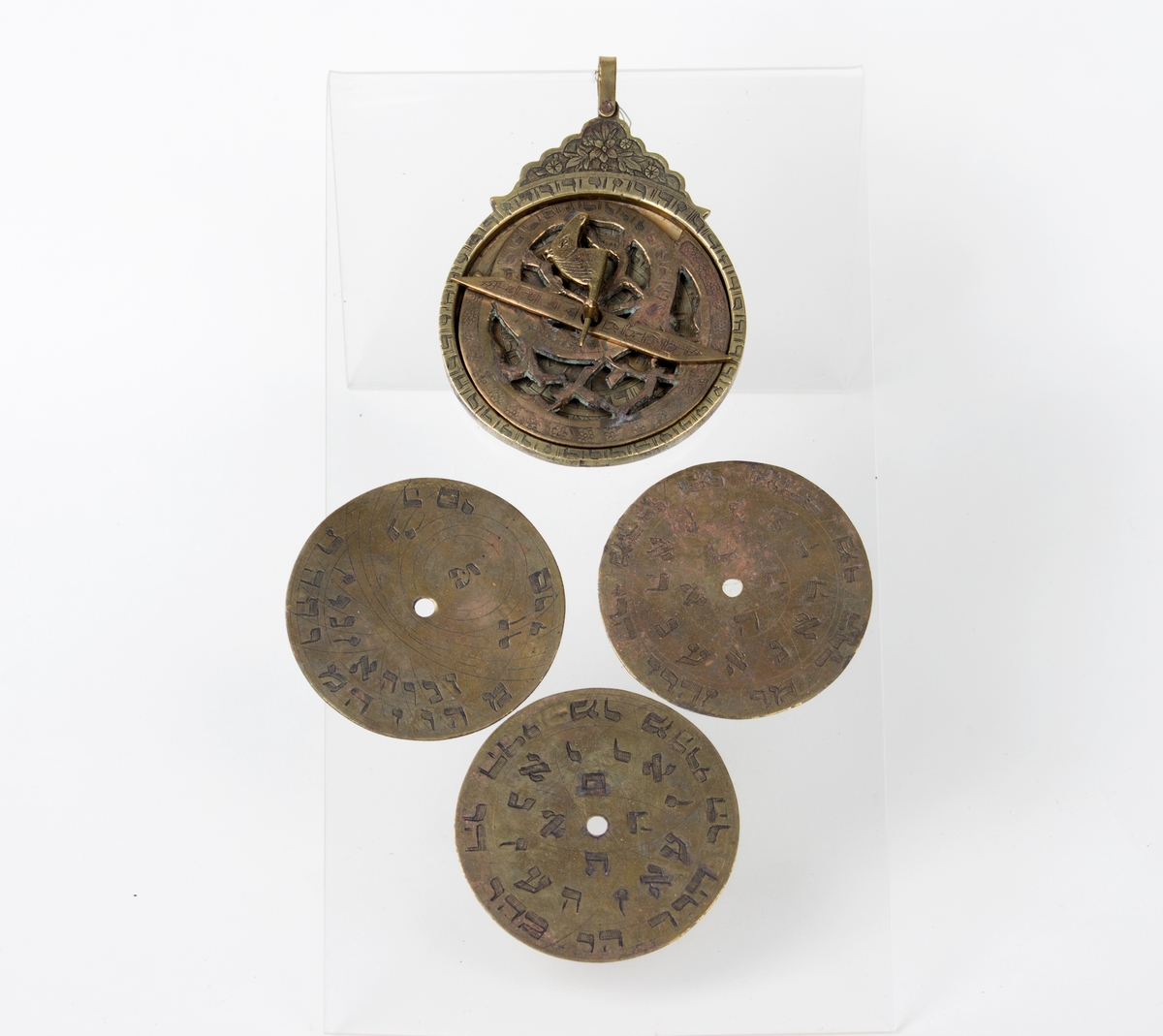 Astrolabium i messing i åtte deler med hebraisk skrifttegn: 5 skiver, 1 viser, 1 stift, 1 pinn m/hestehode. 3 av disse skivene er utstilt sammen med astrolabien.De sirkelformede messingplatene kan skiftes ut og dreies rundt.