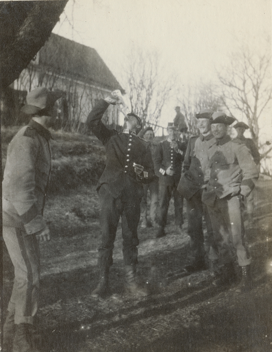 Soldat från Göta livgarde har drickapaus utomhus. Andra soldater med glada miner står omkring.