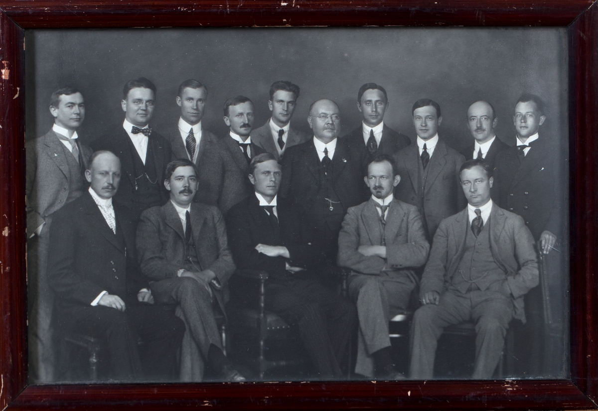 Gruppefoto av møtedeltagere, 15 menn i dress sittende og stående.