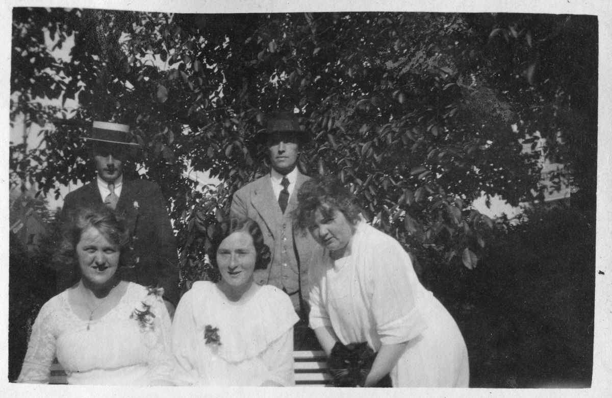 Gruppe mennesker på en benk i hagen ved Grand Hotel, Lillesand 1921. Bildetekst: "Haven, Grand Hotel